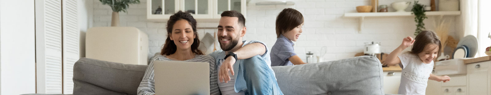 Parents on couch looking at computer with children running around the couch